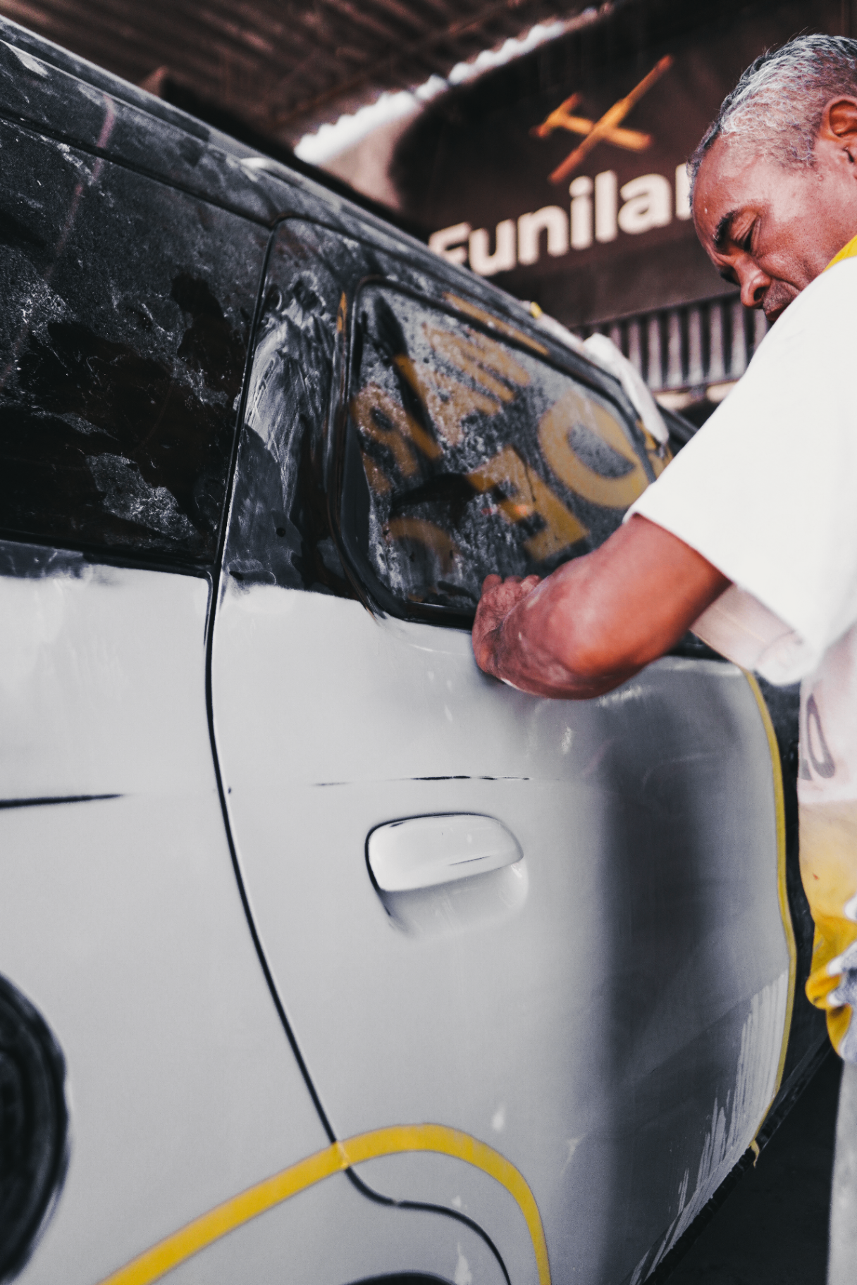 Profissional da Refino Car realizando funilaria em porta de veículo na oficina